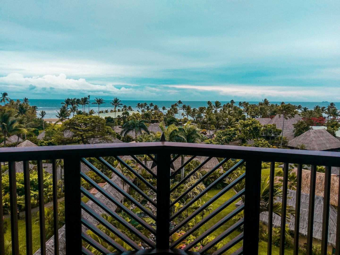 Tropical resort bungalows with thatched roofs and palm trees beside the blue ocean.