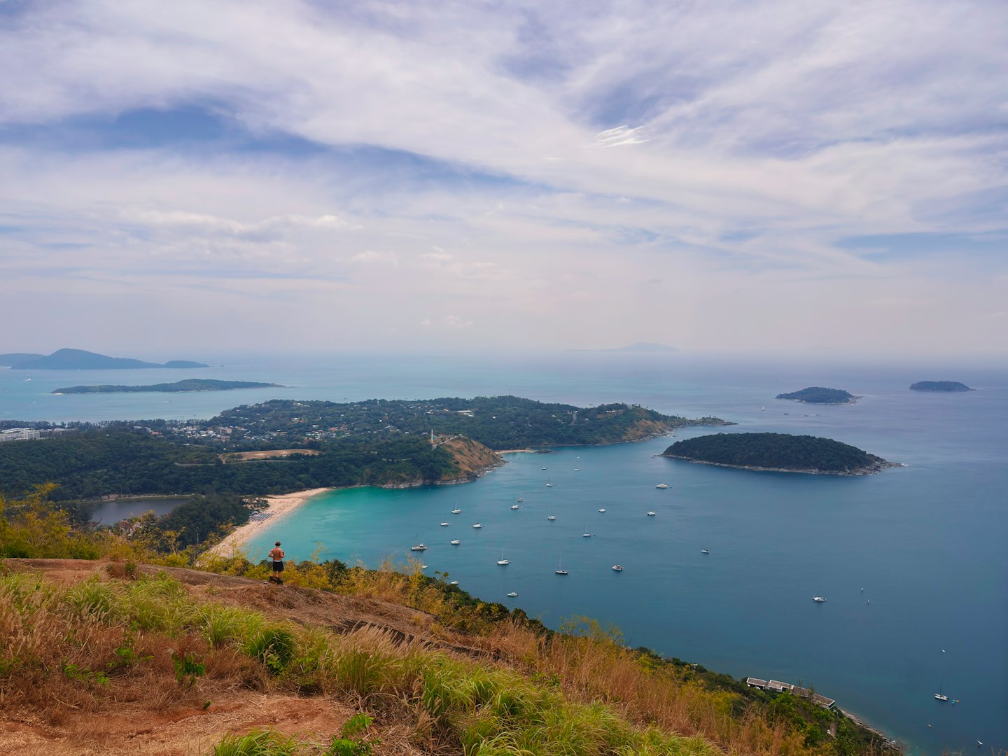 A person stands on a grassy hill overlooking a tropical bay.