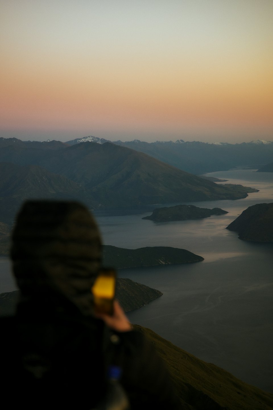 Hiker photographs mountain lake sunrise with smartphone.